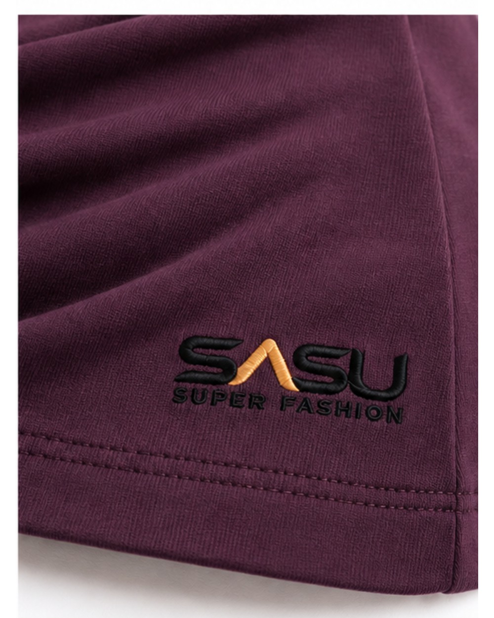 Close-up of the black and gold embroidered logo near the hem of the plum top